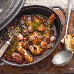 Ein köstliches Coq au Vin ganzes Huhn in dunkler Sauce mit Pilzen und Zwiebeln, serviert in einem Gusseisentopf. Dazu Baguette.