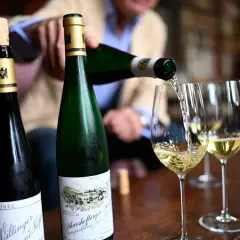 Egon Müller schenkt Wein aus zwei Mosel-Flaschen in Weingläser.