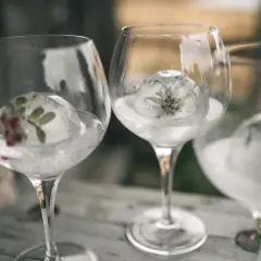 Drei Gläser mit Gin Tonic, gekühlt mit Eisbällen, die Kräuter und Beeren enthalten.