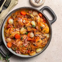 Herzhaftes Coq au Vin in einer Pfanne, mit Hähnchenteilen, Karotten, Zwiebeln und Pilzen in einer reichhaltigen Sauce.