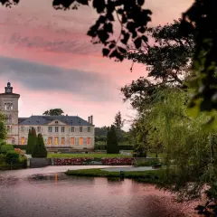 Schloss Saint Julien am See, umgeben von Bäumen, bei Sonnenuntergang mit rosa Himmel.