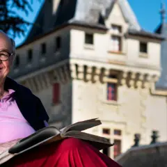 Ein Mann mit Brille liest ein Buch vor dem **Château de Pressac**.