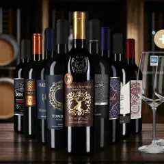 Eine Auswahl an Flaschen Rotwein, die auf einer Holzoberfläche stehen, mit Weinfässern im Hintergrund. Diese Weine könnten Teil einer besten Rotwein Rangliste sein.
