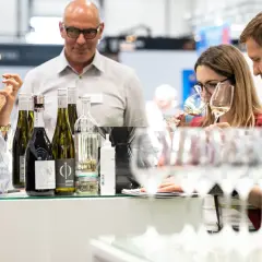 Rheinhessen Winzer präsentieren ihre Weine. Eine Frau verkostet ein Glas, während ein Mann und eine weitere Frau aufmerksam zusehen.