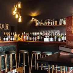 Gemütliche Weinbar mit vielen Flaschen, Barhockern und einer warmen Lampe. Perfekt für einen glasweise Wein.