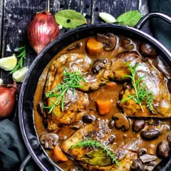 Klassisches Coq au Vin Rezept: Hähnchenteile in reichhaltiger Rotweinsoße mit Pilzen, Karotten und Kräutern.