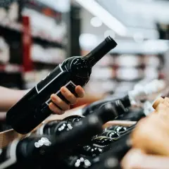 Eine Hand wählt eine Flasche Wein aus, vielleicht ein schmackhafter vin de pays, aus einem Holzkasten voller Flaschen in einem Geschäft.