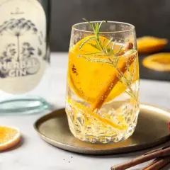 Erfrischendes rezept mit gin: Glas gefüllt mit Gin-Tonic, garniert mit Orangenscheiben, Rosmarin und Zimtstange. Daneben eine Flasche "Herbal Gin".