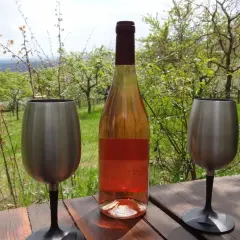 Flasche Roséwein und zwei Edelstahlgläser auf Holztisch, umgeben von blühenden Obstbäumen. Ein echter Geheimtipp von einem Winzer aus der Pfalz.