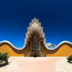 Moderne Weinbodega mit wellenförmiger Fassade und metallischem Dach in Rioja Alavesa, umgeben von Weinbergen und Bergen.