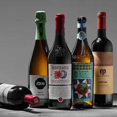 Fünf Flaschen Wein, darunter ein Sekt und vier Rotweine, stehen auf einem Tisch. Einer der Rotweine liegt vorn. Ein Etikett weist auf biodynamischen Wein hin.