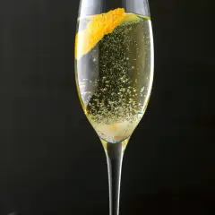 Ein Champagner-Cocktail mit einer Orangenzeste, sprudelnd und erfrischend, vor dunklem Hintergrund.