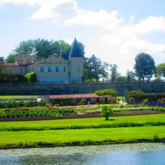 Schloss mit Türmchen und Gartenanlage, davor ein Teich.