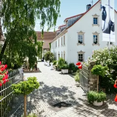 Ein sonniger Tag am Weingut Christian Stahl. Rote Rosen blühen vor dem Tor, eine Frau im roten Kleid betritt das Anwesen.