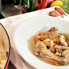 Coq au Riesling nach Martina und Moritz Rezept: Hähnchenteile in cremiger Sauce mit Karotten und Sellerie, daneben ein Kochtopf.