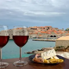 Zwei Gläser Rotwein und eine Käseplatte mit Schinken vor der Kulisse von Dubrovnik. Eine perfekte Weinprobe in Kroatien.