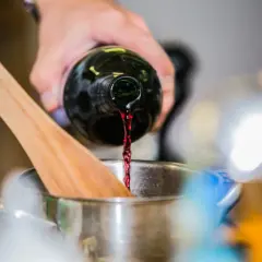 Rotwein wird in einen Topf gegossen, während ein Kochlöffel daneben liegt. Die Frage, wie lange braucht Rotwein zum Verkochen, ist hier relevant.