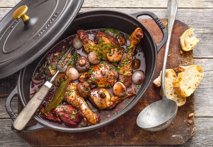 Ein köstliches Coq au Vin ganzes Huhn in dunkler Sauce mit Pilzen und Zwiebeln, serviert in einem Gusseisentopf. Dazu Baguette.