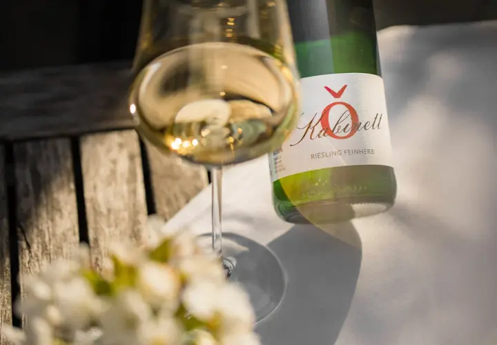 Ein Glas Riesling feinherb, ein Produkt eines Winzers an der Mosel, steht neben der Flasche auf einem Holztisch.