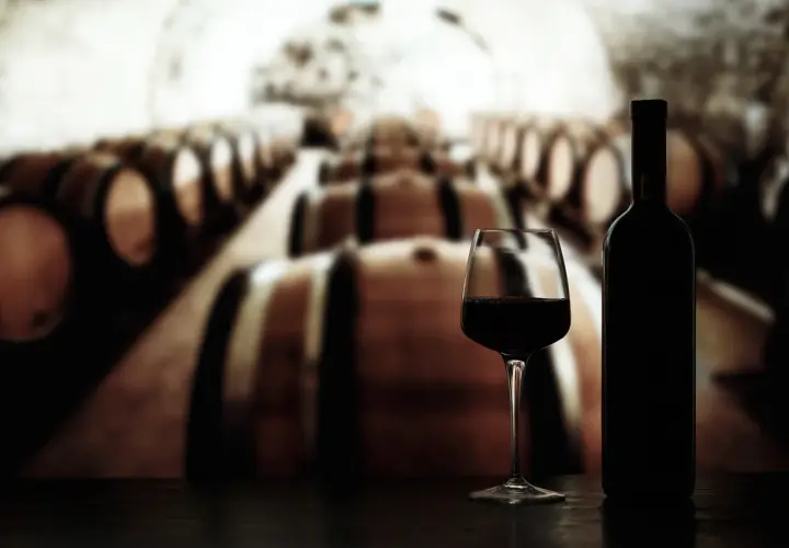 Glas Rotwein und Flasche vor Reihen von Eichenfässern, die auf die Reifung von crianza rioja hindeuten.