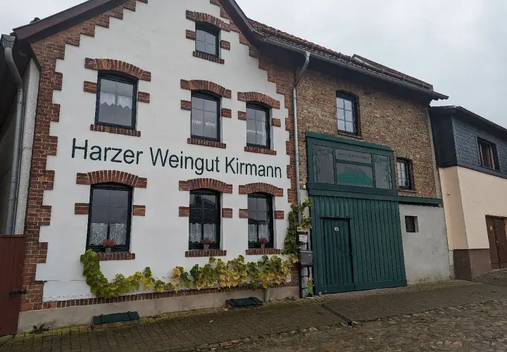 Das Harzer Weingut Kirmann präsentiert sich mit weißer Fassade und roten Ziegelakzenten. Ranken schmücken die Hauswand.