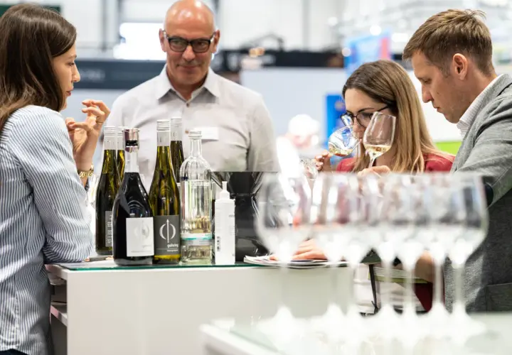 Rheinhessen Winzer präsentieren ihre Weine. Eine Frau verkostet ein Glas, während ein Mann und eine weitere Frau aufmerksam zusehen.