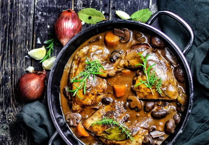 Klassisches Coq au Vin Rezept: Hähnchenteile in reichhaltiger Rotweinsoße mit Pilzen, Karotten und Kräutern.