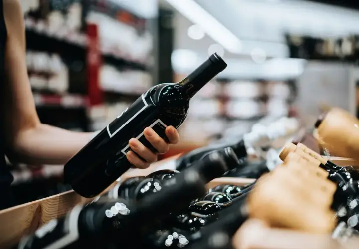 Eine Hand wählt eine Flasche Wein aus, vielleicht ein schmackhafter vin de pays, aus einem Holzkasten voller Flaschen in einem Geschäft.
