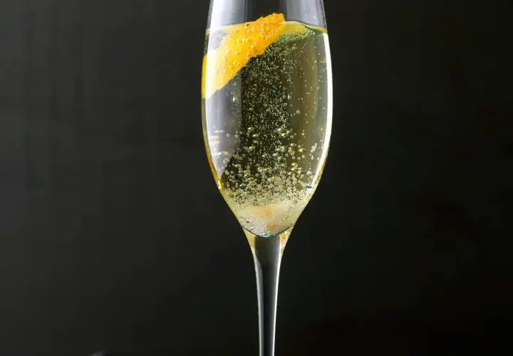 Ein Champagner-Cocktail mit einer Orangenzeste, sprudelnd und erfrischend, vor dunklem Hintergrund.