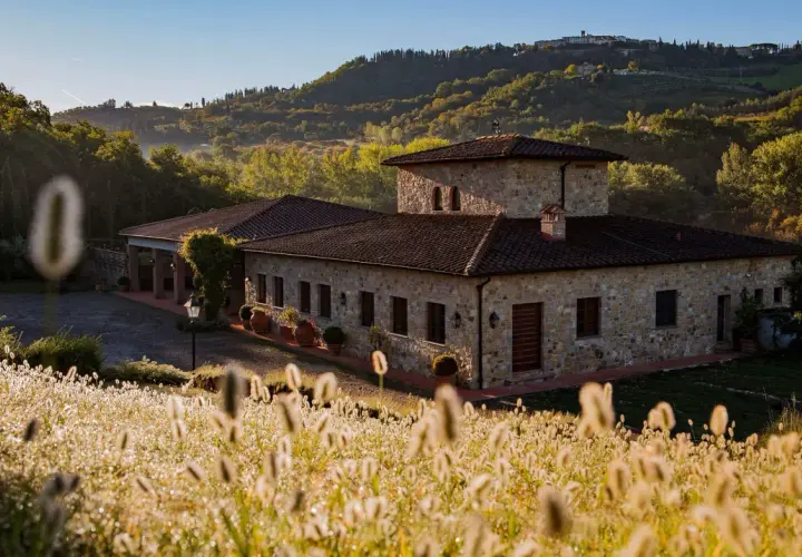 Steinhof mit Ziegeldach im Chianti, umgeben von Hügeln und Gräsern im Morgenlicht.