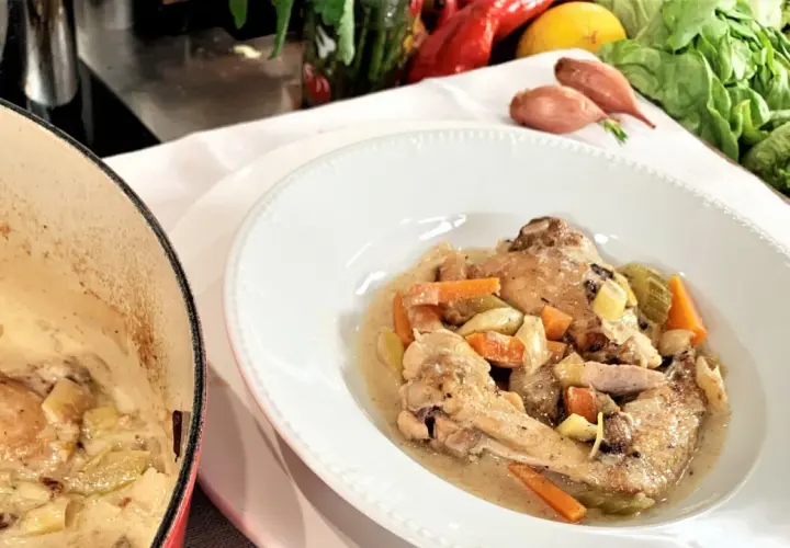 Coq au Riesling nach Martina und Moritz Rezept: Hähnchenteile in cremiger Sauce mit Karotten und Sellerie, daneben ein Kochtopf.