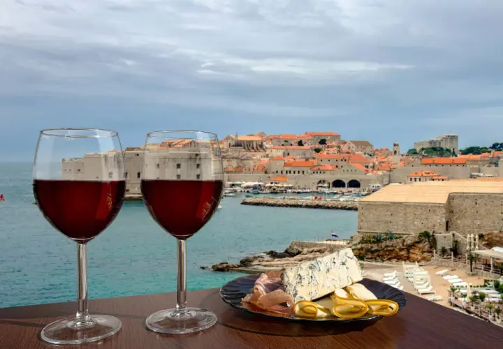 Zwei Gläser Rotwein und eine Käseplatte mit Schinken vor der Kulisse von Dubrovnik. Eine perfekte Weinprobe in Kroatien.