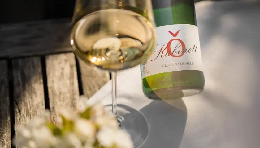 Ein Glas Riesling feinherb, ein Produkt eines Winzers an der Mosel, steht neben der Flasche auf einem Holztisch.