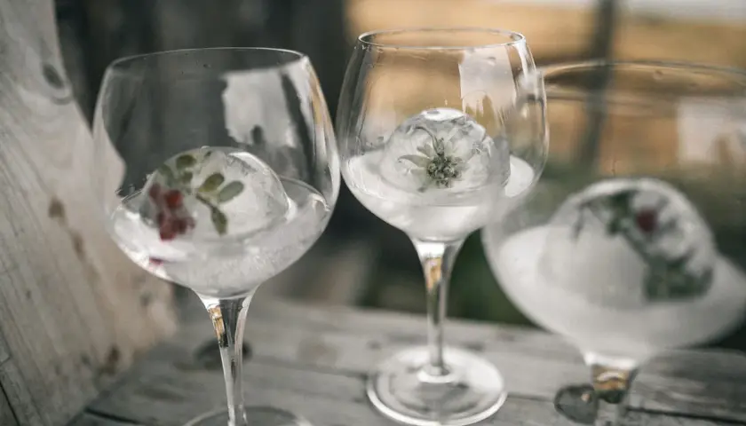 Drei Gläser mit Gin Tonic, gekühlt mit Eisbällen, die Kräuter und Beeren enthalten.