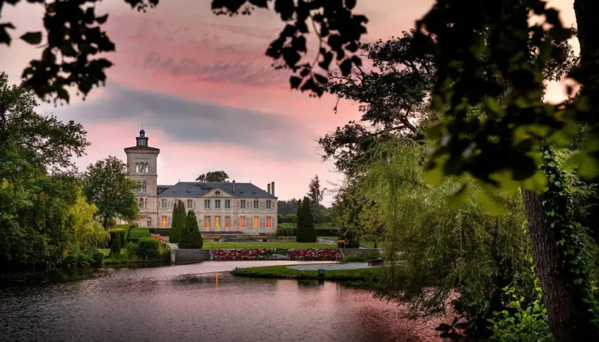 Schloss Saint Julien am See, umgeben von Bäumen, bei Sonnenuntergang mit rosa Himmel.