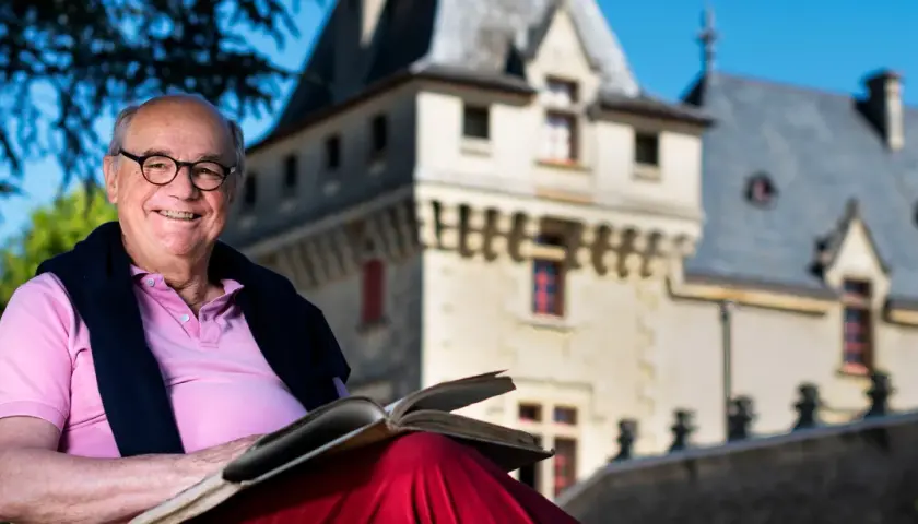Ein Mann mit Brille liest ein Buch vor dem **Château de Pressac**.