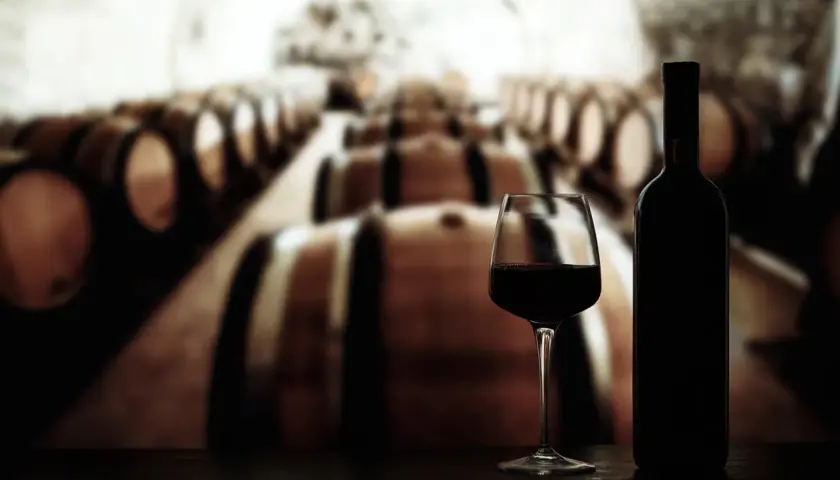 Glas Rotwein und Flasche vor Reihen von Eichenfässern, die auf die Reifung von crianza rioja hindeuten.