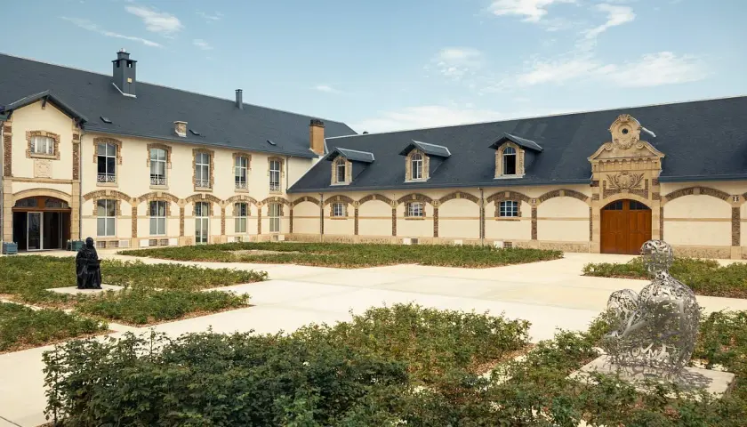Der Innenhof von Maison Ruinart mit moderner Skulptur und grünen Büschen.