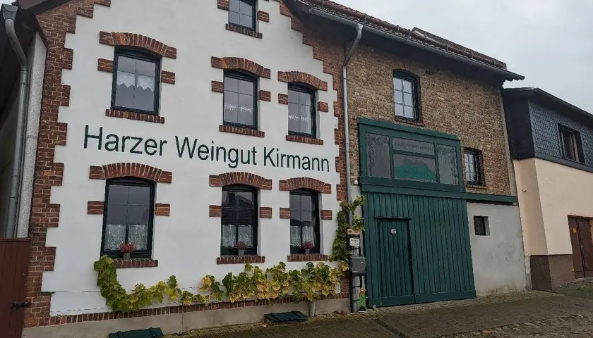 Das Harzer Weingut Kirmann präsentiert sich mit weißer Fassade und roten Ziegelakzenten. Ranken schmücken die Hauswand.