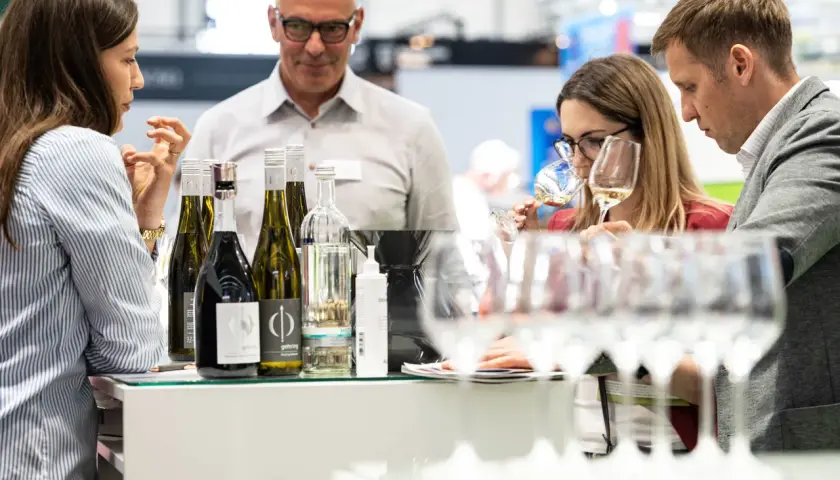 Rheinhessen Winzer präsentieren ihre Weine. Eine Frau verkostet ein Glas, während ein Mann und eine weitere Frau aufmerksam zusehen.