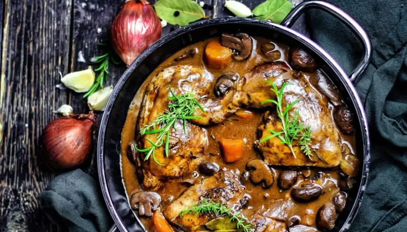 Klassisches Coq au Vin Rezept: Hähnchenteile in reichhaltiger Rotweinsoße mit Pilzen, Karotten und Kräutern.