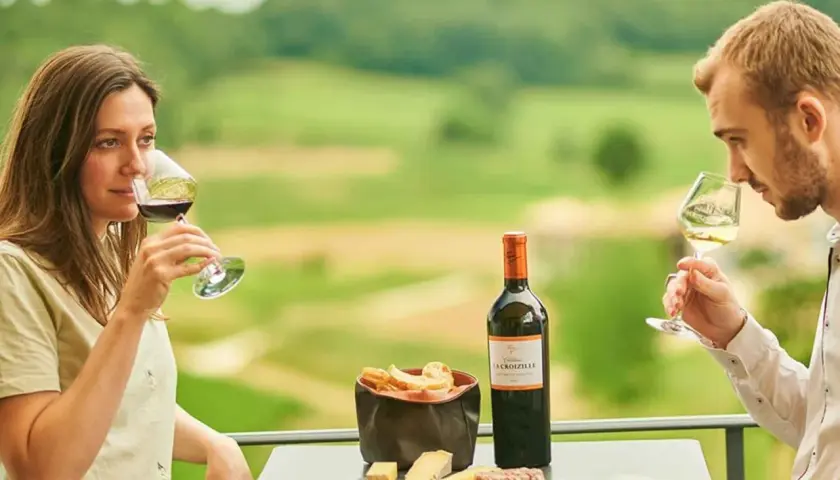 Ein Paar genießt Wein und Käse auf der Terrasse eines Weinguts in Bordeaux. Die Weinprobe verspricht Genuss.