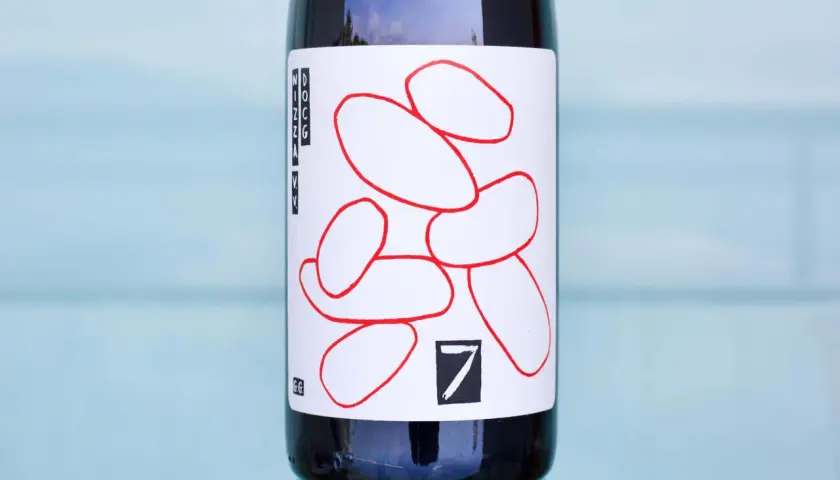 Flasche mit Etikett, das rote, abstrakte Formen und die Aufschrift "Nizza Monferrato" zeigt.