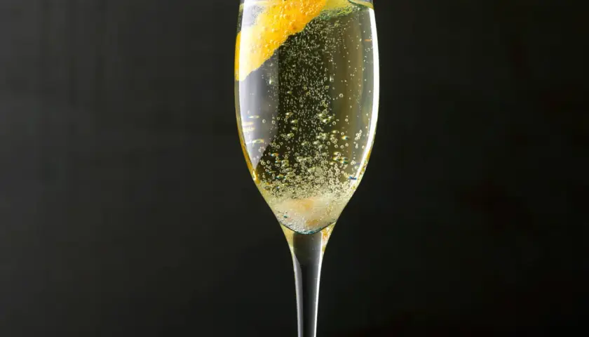 Ein Champagner-Cocktail mit einer Orangenzeste, sprudelnd und erfrischend, vor dunklem Hintergrund.
