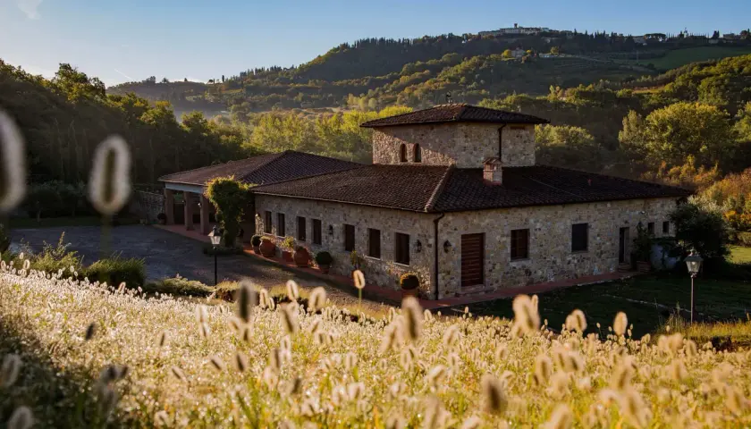 Steinhof mit Ziegeldach im Chianti, umgeben von Hügeln und Gräsern im Morgenlicht.