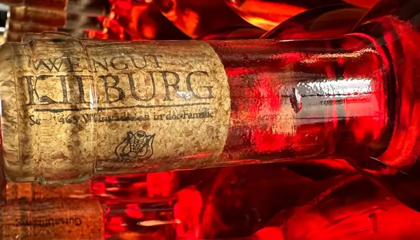 Rotwein-Flasche mit dem Etikett "Weingut Kilburg" im Vordergrund. Ein typischer Mosel Wein, der in der Sonne glänzt.