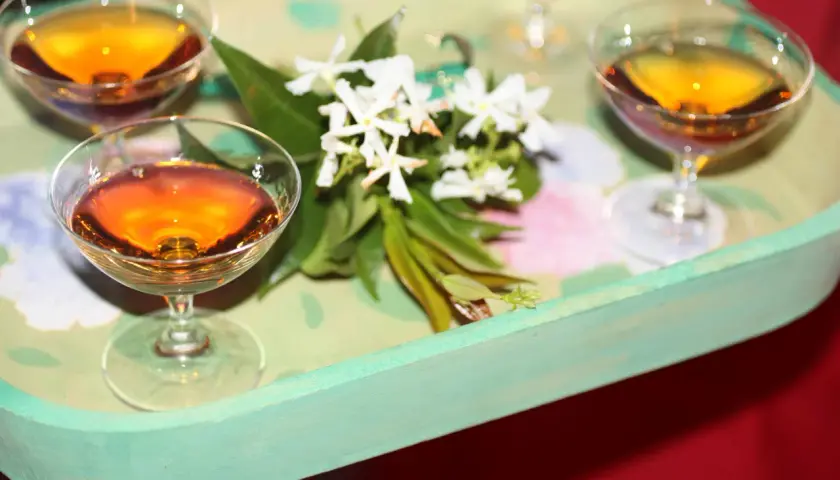 Bernsteinfarbene Likörgläser auf einem Tablett mit Blumen. Eine elegante Alternative zu Vin Santo für besondere Anlässe.