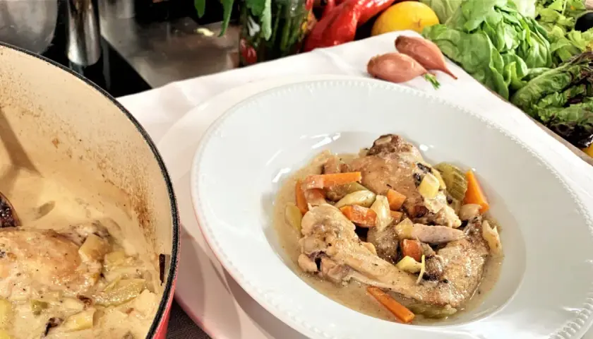 Coq au Riesling nach Martina und Moritz Rezept: Hähnchenteile in cremiger Sauce mit Karotten und Sellerie, daneben ein Kochtopf.