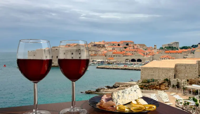 Zwei Gläser Rotwein und eine Käseplatte mit Schinken vor der Kulisse von Dubrovnik. Eine perfekte Weinprobe in Kroatien.