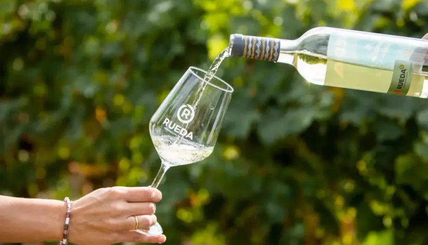 Ein Glas wird mit Weißwein gefüllt, der aus einer Flasche mit dem Etikett "Rueda" gegossen wird. Ein Hauch von verdejo deutsch in der Luft.